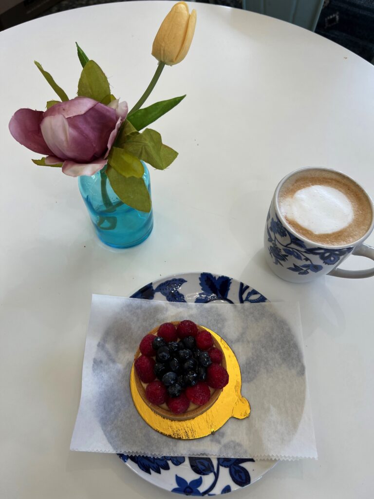 Raspberry and blueberry crême fraiche tart, frothy cappuccino in a mug with blue flowers, and a purple flower in a blue bottle.